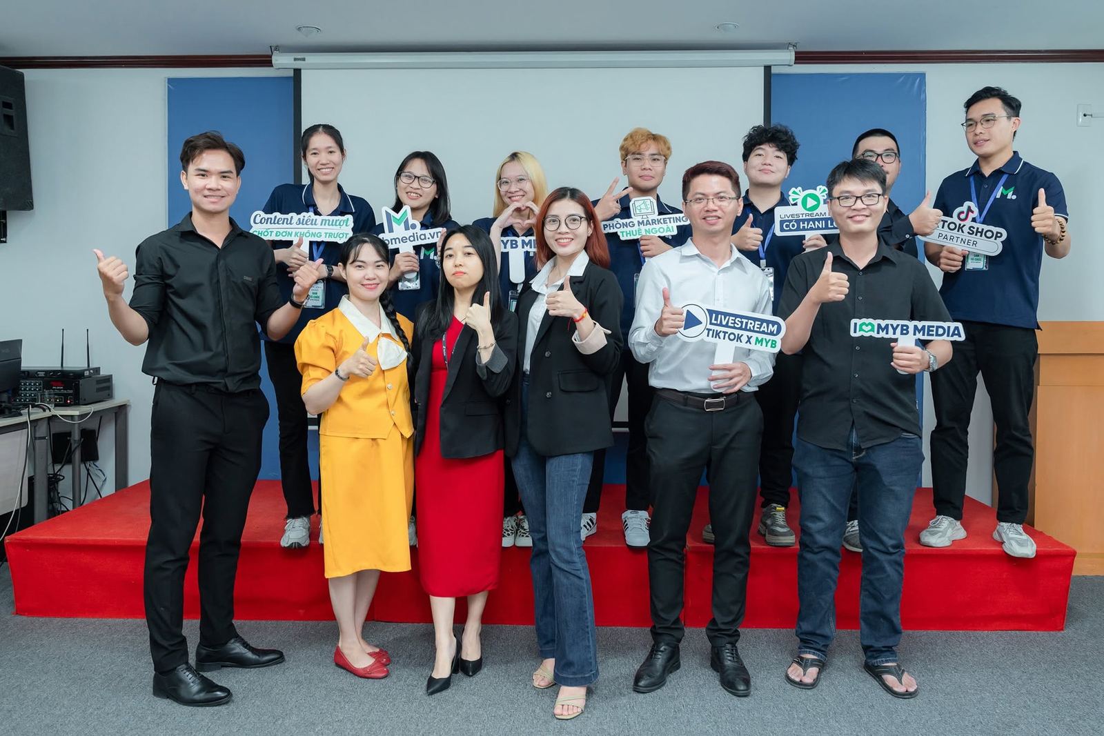 Đội ngũ MYB trên sân khấu, với các biển content, phòng marketing thuê ngoài, livestream và TikTok Shop.